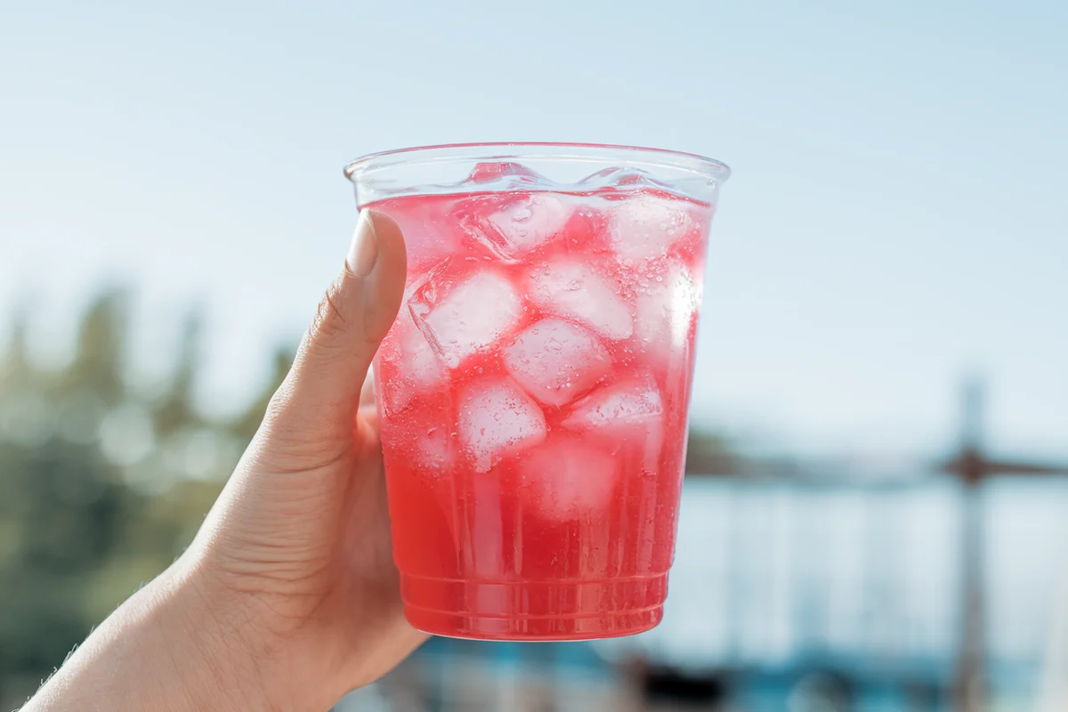 Hand holding a bright pink fruity drink with ice cubes.