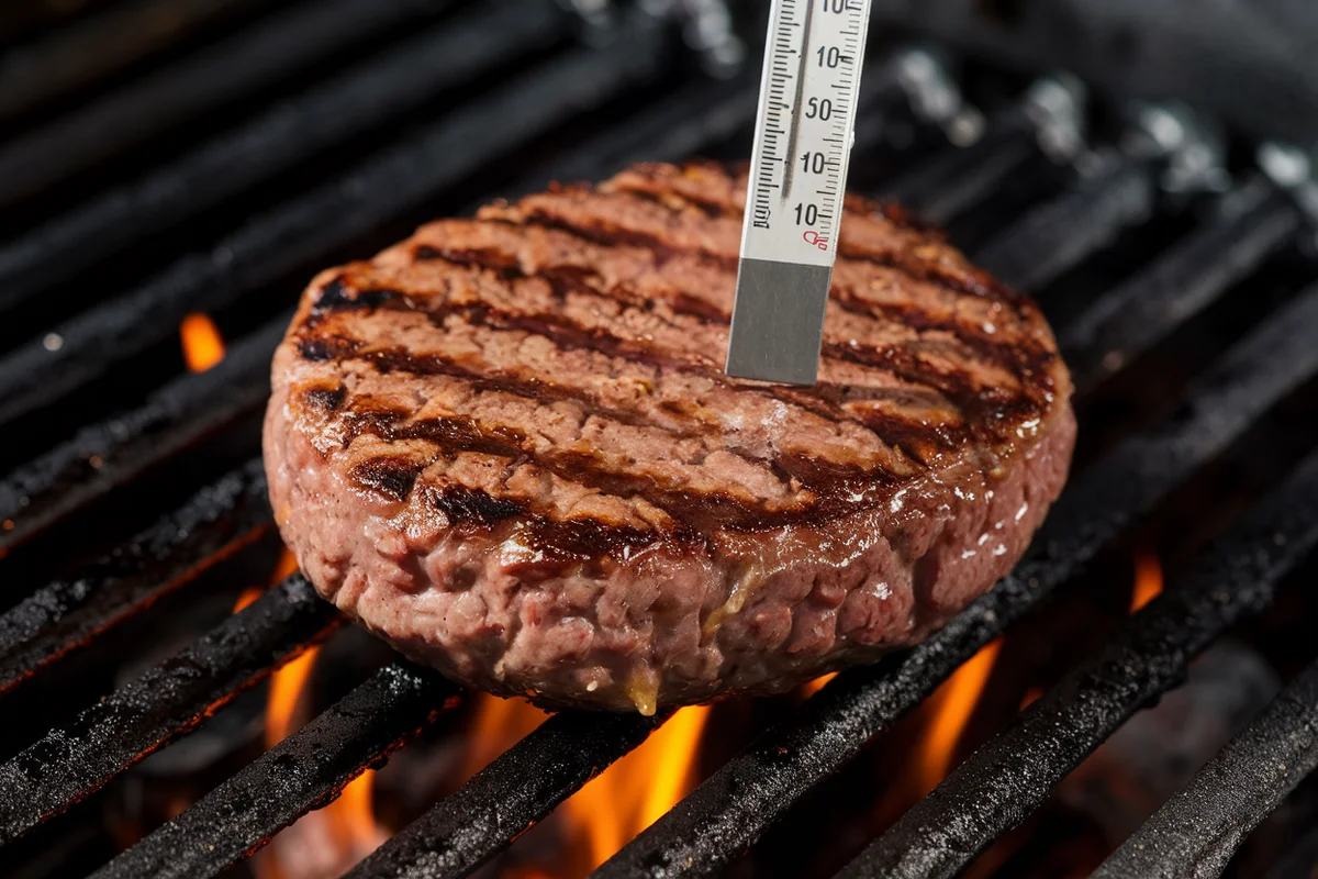 Burger patty on a grill with a thermometer showing 150 degrees Fahrenheit.